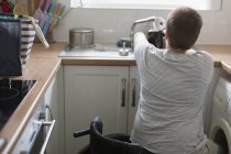 Junge Frau im Rollstuhl füllt Wasserkocher für Tee an Wohnküche-Spüle — Stockfoto