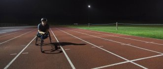 Портрет уверенный, целеустремленный молодой парализованной спортсменки подготовка к гонке на инвалидных колясках на спортивной трассе ночью — стоковое фото