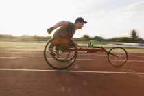Adolescente menino atleta paraplégico acelerando ao longo da pista de esportes em corrida de cadeira de rodas — Fotografia de Stock