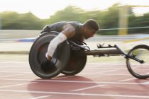 Entschlossener junger querschnittsgelähmter Sportler rast im Rollstuhlrennen über Sportbahn — Stockfoto