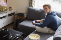 Selbstbewusste junge Frau spielt Videospiel auf Sofa neben Rollstuhl — Stockfoto