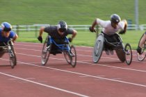 Atleta paraplegico determinato che accelera lungo la pista sportiva in gara su sedia a rotelle — Foto stock
