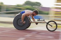 Determinado joven masculino parapléjico exceso de velocidad en pista deportiva en la carrera en silla de ruedas - foto de stock