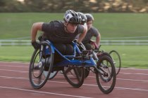 Deportista parapléjica joven decidida a correr a lo largo de la pista deportiva en la carrera en silla de ruedas - foto de stock