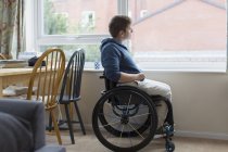 Jovem mulher pensativa em cadeira de rodas olhando pela janela — Fotografia de Stock