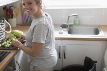 Retrato sorrindo jovem com cadeira de rodas cortando legumes na cozinha do apartamento — Fotografia de Stock