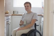 Портрет уверенная молодая женщина в инвалидной коляске пьет чай на кухне квартиры — стоковое фото