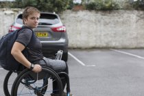 Portrait confiant jeune étudiante universitaire en fauteuil roulant dans le stationnement — Photo de stock