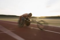 Determinato giovane atleta paraplegico maschile che corre lungo la pista sportiva in gara su sedia a rotelle — Foto stock