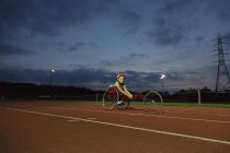 Ritratto fiducioso adolescente atleta paraplegico formazione per gara sedia a rotelle su pista sportiva di notte — Foto stock