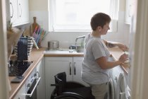 Jovem com cadeira de rodas na cozinha do apartamento — Fotografia de Stock
