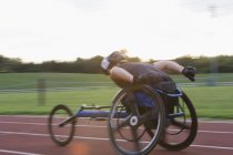 Atleta paraplegico che accelera lungo la pista sportiva in gara su sedia a rotelle — Foto stock