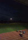 Atletas paraplégicos acelerando ao longo da pista de esportes em corrida de cadeira de rodas à noite — Fotografia de Stock