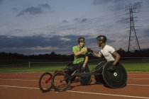 Paraplegic athletes fist bumping on sports track, training for wheelchair race at night — Stock Photo
