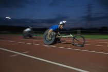 Визначений молодий чоловічий паралельний спортсмен, що перевищує швидкість вздовж спортивної траси в гонці на інвалідних візках вночі — стокове фото