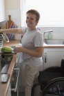 Портрет улыбается молодая женщина с инвалидной коляской приготовления пищи в квартире кухне — стоковое фото