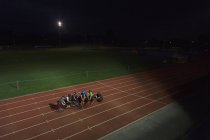 Atletas parapléjicos en pista deportiva, entrenamiento para la carrera en silla de ruedas por la noche - foto de stock