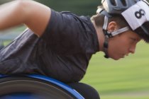 Athlète paraplégique féminine déterminée accélérant le long de la piste de sport pendant la course en fauteuil roulant — Photo de stock