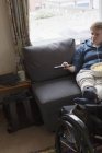 Молодая женщина смотрит телевизор с поднятыми ногами на инвалидной коляске — стоковое фото