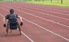 Atleta paraplegica femminile che accelera lungo la pista sportiva in gara su sedia a rotelle — Foto stock