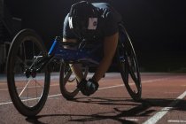 Atleta parapléjico cansado descansando en pista deportiva después de la carrera en silla de ruedas por la noche - foto de stock
