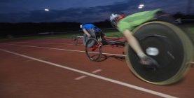 Паралитические спортсмены, мчащиеся по спортивной трассе в гонке на инвалидных колясках ночью — стоковое фото
