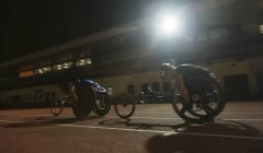 Паралитические спортсмены, мчащиеся по спортивной трассе в гонке на инвалидных колясках ночью — стоковое фото