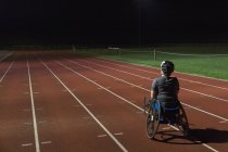 Entrenamiento de atleta parapléjico femenino determinado para la carrera en silla de ruedas en pista deportiva por la noche - foto de stock