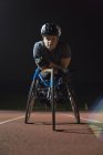 Retrato determinado, duro joven mujer atleta parapléjico entrenamiento para la carrera en silla de ruedas en pista deportiva por la noche - foto de stock