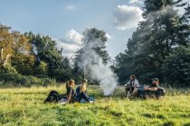 Friends camping, relaxing around campfire in remote field — Stock Photo