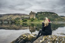 Женщина, наслаждающаяся видом на отдаленный замок на берегу моря, Шотландия — стоковое фото