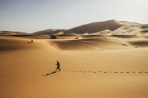 Uomo che cammina nel soleggiato deserto sabbioso, Sahara, Marocco — Foto stock