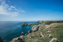 Woman standing on sunny cliffs with ocean view, Cornwall, UK — Stock Photo