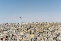 Bandera jordana que ondea sobre edificios soleados de la ciudad, Ammán, Jordania - foto de stock