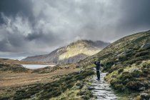 Hombre en camino de piedra entre el paisaje remoto y tranquilo, Snowdonia NP, Reino Unido - foto de stock