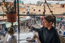 Mulher desfrutando de chá na varanda com vista para o mercado de rua, Marraquexe, Marrocos — Fotografia de Stock
