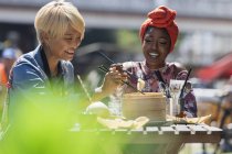 Молодые женщины-подружки наслаждаются обедом с палочками для еды в солнечном кафе на тротуаре — стоковое фото