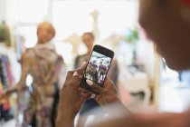 Mujer joven con cámara de teléfono fotografiando amigos de compras en la tienda - foto de stock