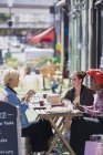 Молодые женщины-друзья наслаждаются обедом дим в солнечном кафе на тротуаре — стоковое фото