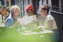 Young women friends looking at map, enjoying lunch at sunny sidewalk cafe — Stock Photo