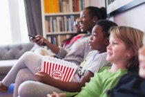 Family and friends watching movie and eating popcorn on living room sofa — Stock Photo