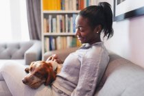 Молода жінка сміється з собакою на дивані у вітальні — стокове фото