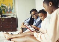Familia multigeneración que utiliza tableta digital en la cama - foto de stock