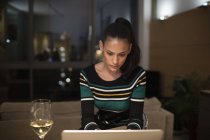 Зосереджена жінка п'є біле вино і працює в ноутбуці вночі — стокове фото