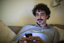 Homem usando telefone inteligente no sofá à noite — Fotografia de Stock