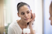 Frau trägt Feuchtigkeitscreme auf Gesicht im Badezimmerspiegel auf — Stockfoto