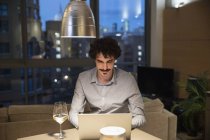 Man using laptop and drinking white wine in urban apartment kitchen at night — Stock Photo