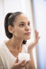 Woman applying moisturizer to face in mirror — Stock Photo