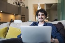 Sorrindo homem usando laptop no sofá apartamento — Fotografia de Stock