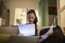 Donna che legge scartoffie, lavora al computer portatile sul divano — Foto stock